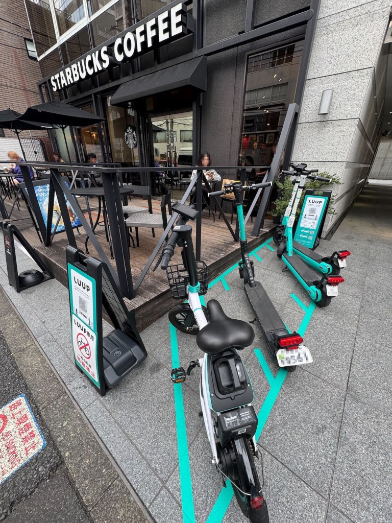 スターバックスコーヒー店舗前に設置されたLUUPのポート。緑色のラインで区画された駐輪スペースには電動アシスト自転車と電動キックボードが数台駐車されており、近くにLUUPの利用案内看板が設置されている。